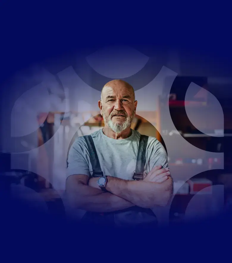 A deep blue background covers the top of the page, with a watermarked version of the hexagonal logo shape overlaid on an image of a mature man wearing a hat, with his arms crossed standing in a workshop, looking confident and in control.